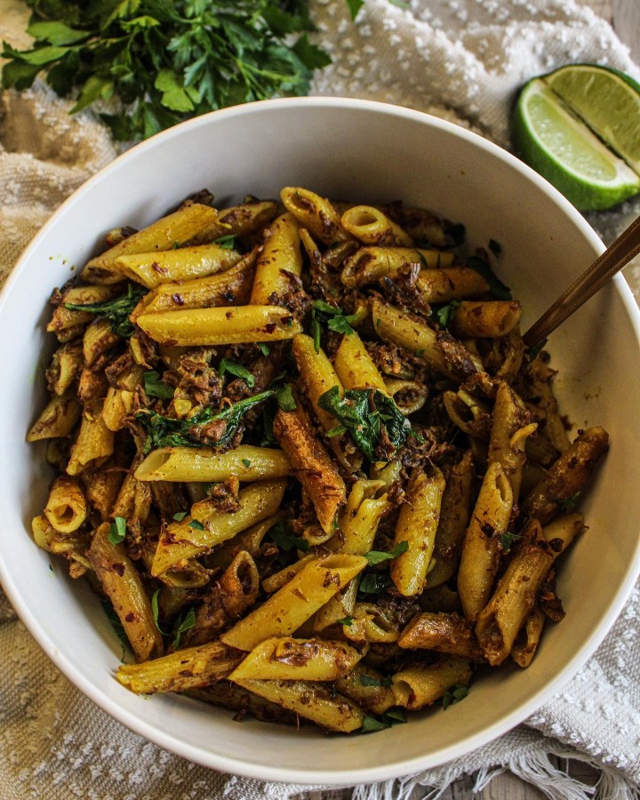 Curried jackfruit penne pasta in a bowl topped with cilantro and lime